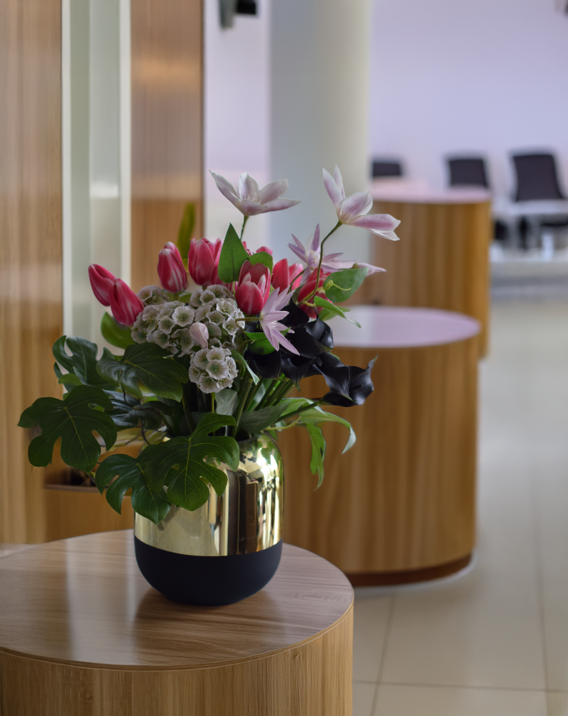 病院の廊下の一角に飾られたアーティフィシャルフラワーによる、金の器に、チューリップやクレマチス、スカビオサ、カラーリリーのインテリアフラワー。